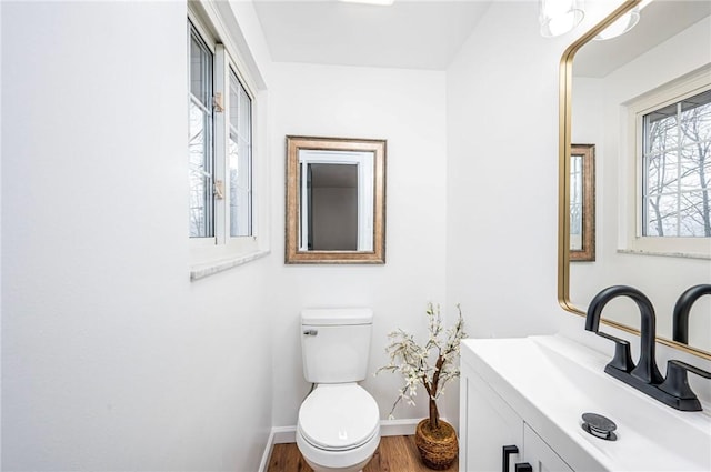 half bathroom featuring toilet, baseboards, wood finished floors, and vanity