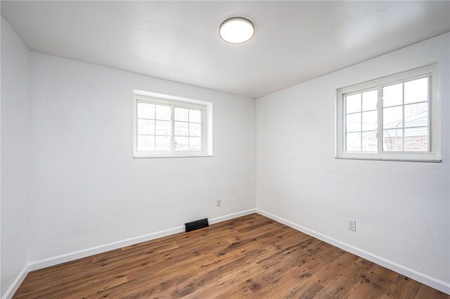 spare room with a healthy amount of sunlight, visible vents, baseboards, and wood finished floors