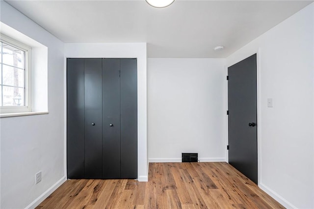 unfurnished bedroom with a closet, visible vents, baseboards, and wood finished floors