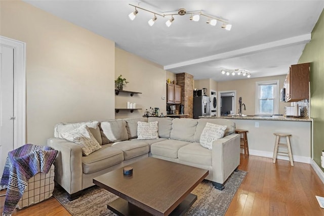 living area featuring light wood-type flooring, beamed ceiling, and baseboards