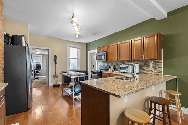 kitchen featuring stainless steel appliances, tasteful backsplash, brown cabinetry, a sink, and a peninsula