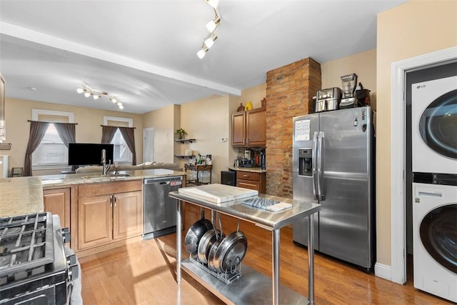 kitchen featuring stacked washer and clothes dryer, stainless steel appliances, light wood-style flooring, open floor plan, and a sink