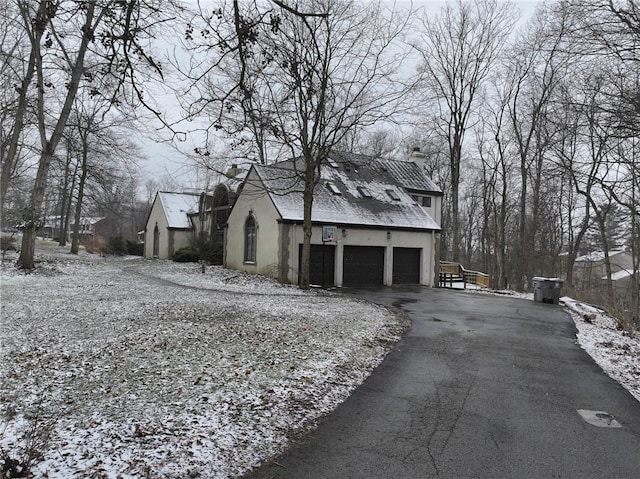 exterior space with aphalt driveway, a chimney, a garage, and stucco siding