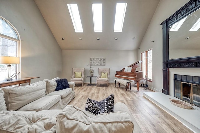 living area with high vaulted ceiling, a glass covered fireplace, a skylight, and wood finished floors