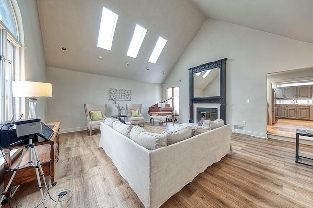 living area featuring high vaulted ceiling, baseboards, a tiled fireplace, and light wood finished floors