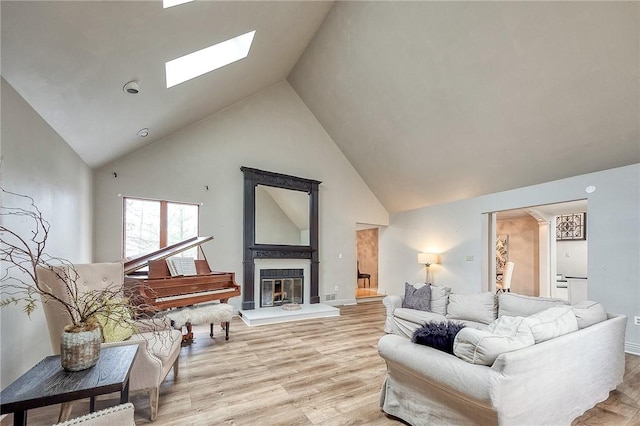 living area featuring light wood-type flooring, a skylight, high vaulted ceiling, and a glass covered fireplace