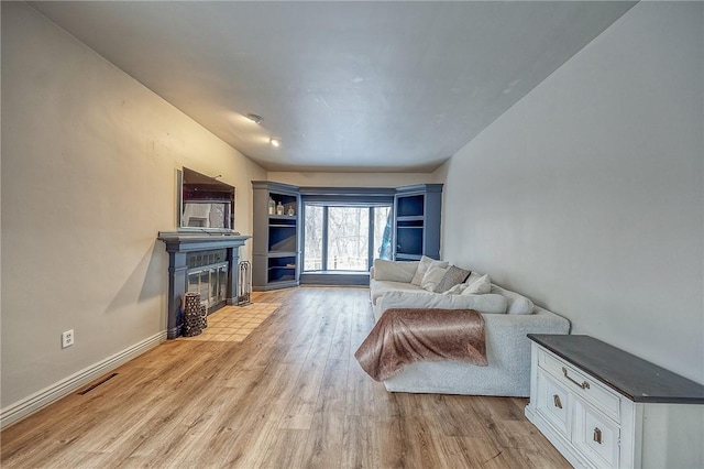 living room featuring light wood-style flooring, visible vents, baseboards, and a fireplace with flush hearth