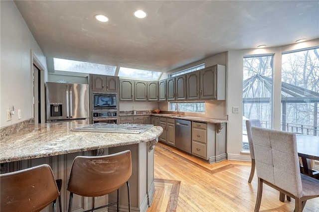 kitchen featuring plenty of natural light, a peninsula, stainless steel appliances, light wood-style floors, and a sink