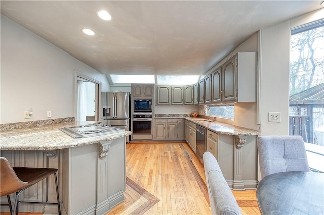 kitchen featuring light wood finished floors, a breakfast bar, a peninsula, stainless steel appliances, and gray cabinetry