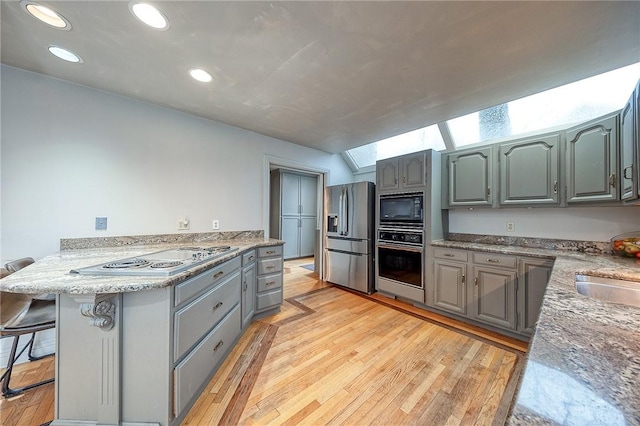 kitchen featuring light wood-style flooring, a peninsula, a breakfast bar, appliances with stainless steel finishes, and gray cabinets