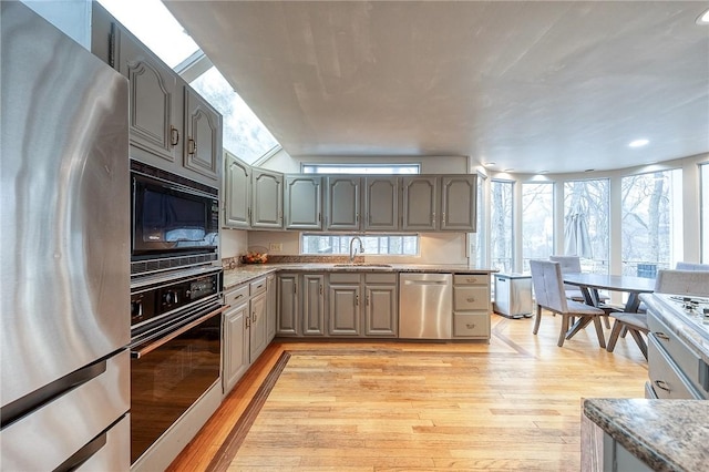 kitchen with light wood-style floors, light stone counters, gray cabinets, black appliances, and a sink