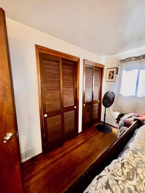 bedroom with multiple closets, baseboards, visible vents, and wood finished floors