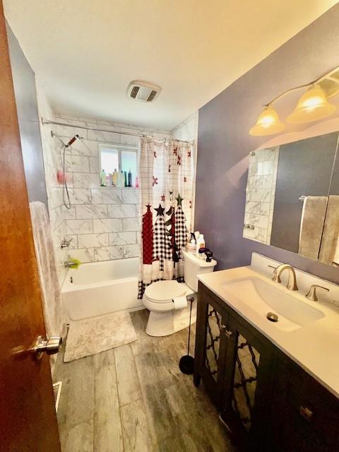 full bath featuring toilet, wood finished floors, vanity, visible vents, and shower / bathtub combination with curtain