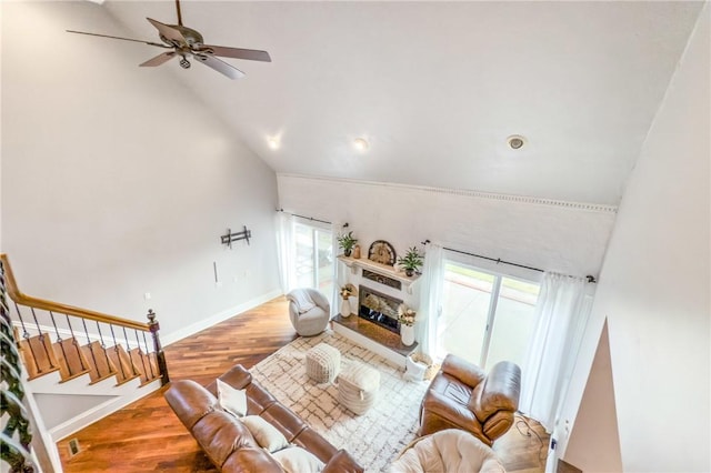 living room with a fireplace with raised hearth, stairway, wood finished floors, high vaulted ceiling, and baseboards