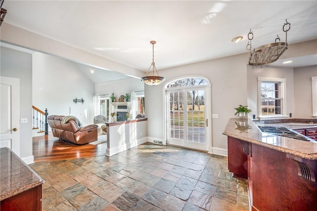 kitchen with stone tile floors, hanging light fixtures, stone countertops, vaulted ceiling, and baseboards