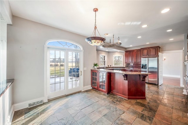 kitchen featuring stainless steel refrigerator with ice dispenser, baseboards, visible vents, a peninsula, and a kitchen breakfast bar