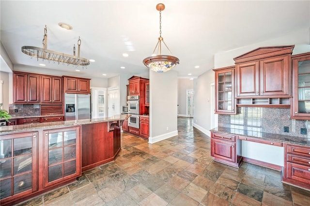 kitchen featuring light stone counters, stainless steel appliances, hanging light fixtures, decorative backsplash, and baseboards