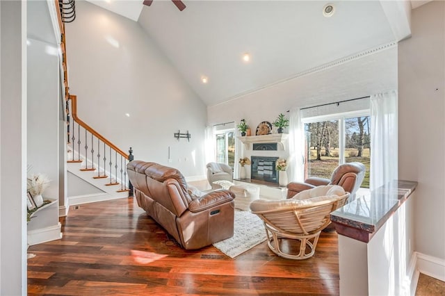 living area with high vaulted ceiling, wood finished floors, baseboards, stairway, and a glass covered fireplace