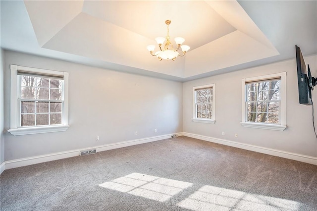 carpeted spare room with plenty of natural light, an inviting chandelier, visible vents, and a tray ceiling