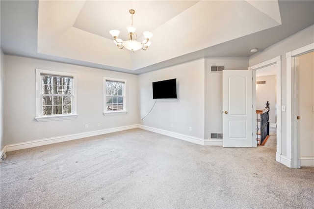 carpeted empty room featuring a tray ceiling, visible vents, baseboards, and an inviting chandelier