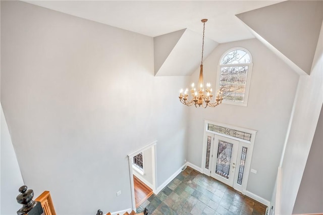 foyer with stone finish floor, an inviting chandelier, baseboards, and vaulted ceiling