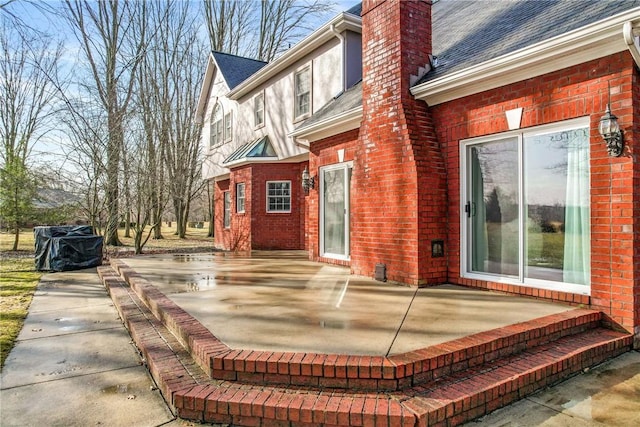 back of property with brick siding, a chimney, a patio area, and a shingled roof