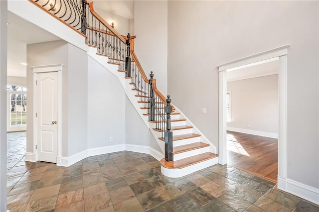 stairs featuring a towering ceiling, stone tile flooring, and baseboards