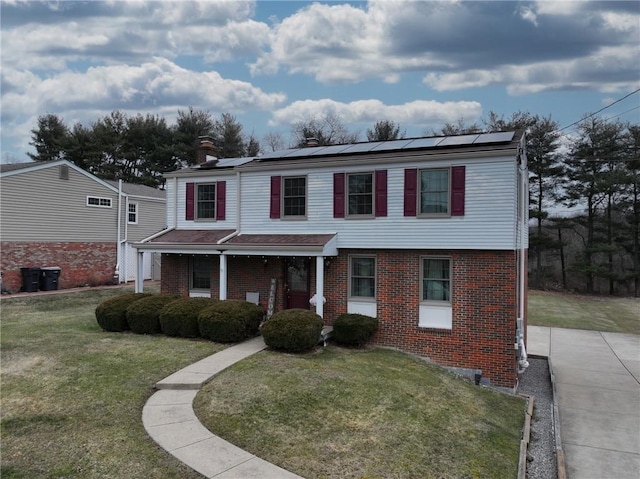 view of front of property featuring solar panels, brick siding, a porch, and a front yard