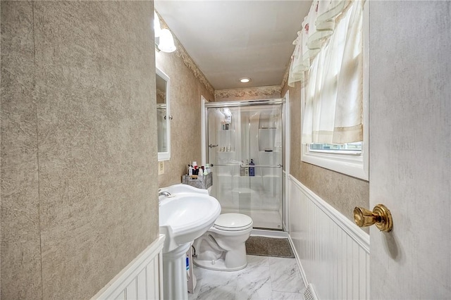 full bath with marble finish floor, a decorative wall, toilet, a stall shower, and wainscoting