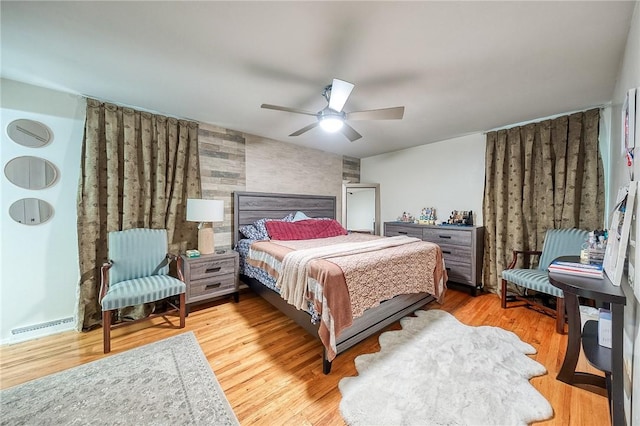 bedroom with a ceiling fan, an accent wall, visible vents, and wood finished floors