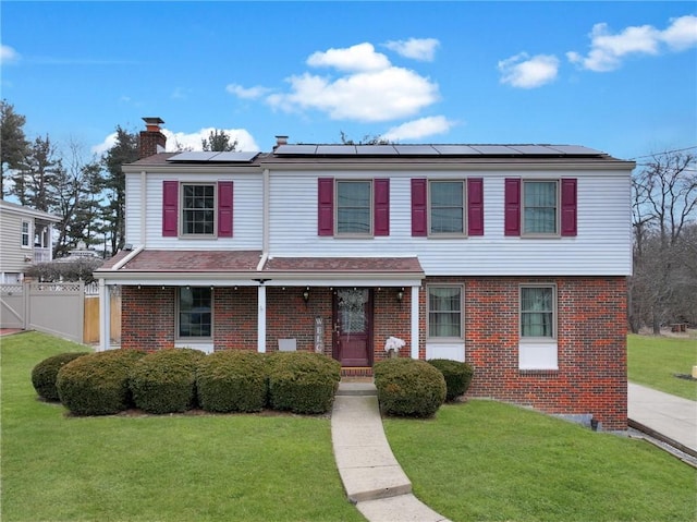 view of front facade with brick siding, a front lawn, a chimney, and fence