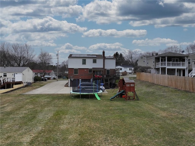 rear view of property with a playground, fence, a lawn, a residential view, and a trampoline