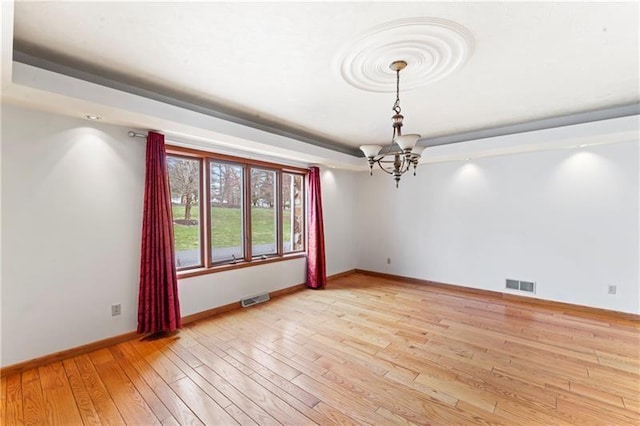 spare room with light wood-style floors, visible vents, and a tray ceiling