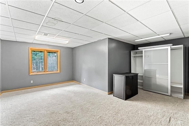 basement featuring baseboards, a drop ceiling, and carpet flooring