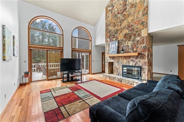 living room with high vaulted ceiling, a stone fireplace, baseboards, and hardwood / wood-style flooring