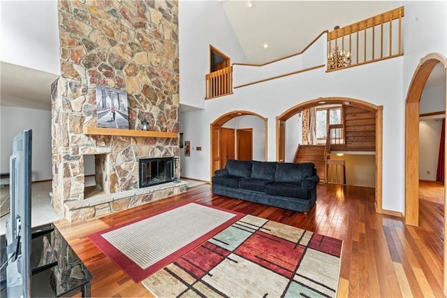 living area with arched walkways, hardwood / wood-style flooring, stairway, a stone fireplace, and high vaulted ceiling