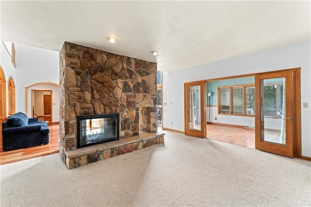 carpeted living room with baseboards, a fireplace, and arched walkways