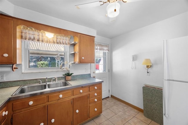 kitchen with light tile patterned floors, baseboards, brown cabinetry, freestanding refrigerator, and a sink