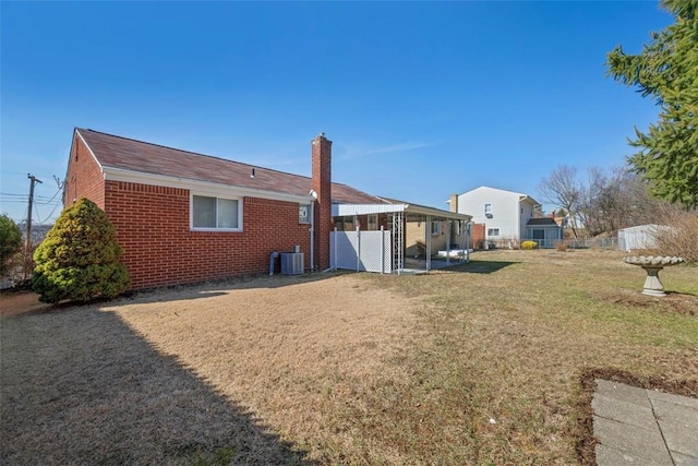 back of property featuring central AC unit, brick siding, fence, a lawn, and a chimney