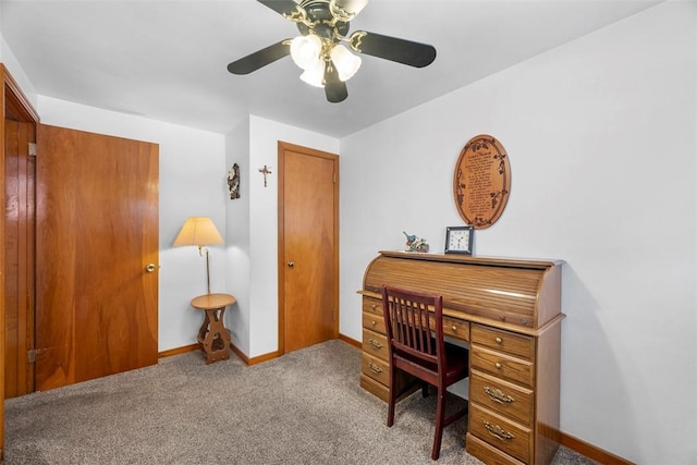 carpeted office space featuring ceiling fan and baseboards