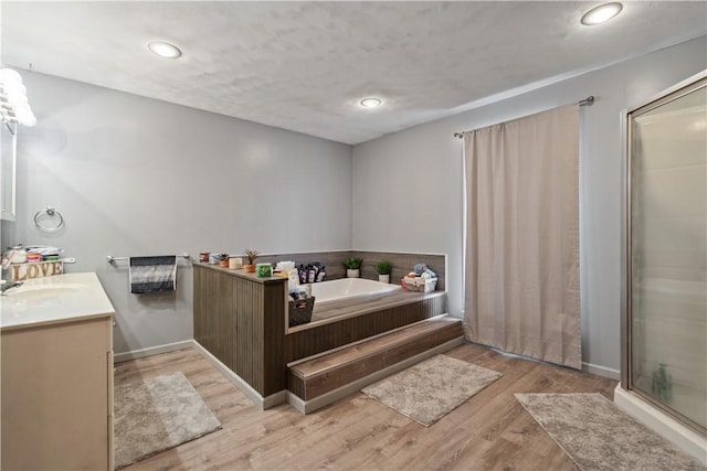 bathroom with a stall shower, baseboards, wood finished floors, vanity, and a bath