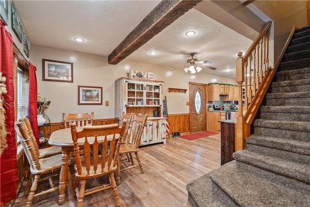 dining space with wooden walls, stairs, light wood-type flooring, wainscoting, and beam ceiling