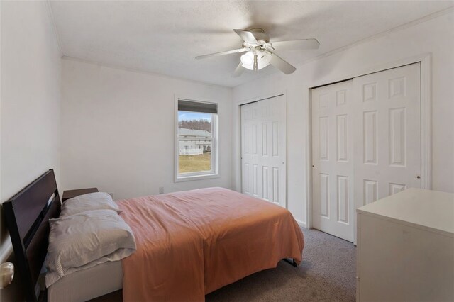 bedroom featuring ornamental molding, carpet, ceiling fan, and two closets