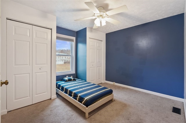 carpeted bedroom with a textured ceiling, ceiling fan, visible vents, multiple closets, and baseboards