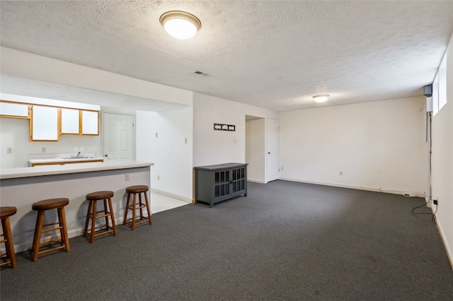 interior space with baseboards, light countertops, a textured ceiling, a kitchen bar, and dark carpet