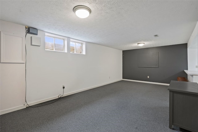 basement with a textured ceiling, dark colored carpet, and baseboards