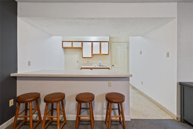 kitchen with a breakfast bar, light countertops, dark carpet, a peninsula, and baseboards