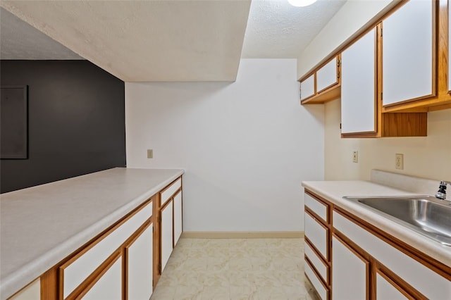 kitchen with a textured ceiling, light countertops, a sink, and baseboards