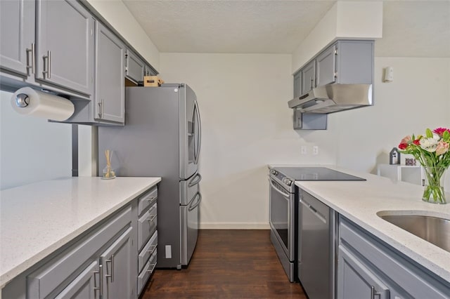 kitchen with light stone counters, under cabinet range hood, dark wood-style flooring, appliances with stainless steel finishes, and gray cabinets