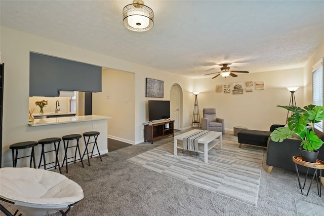 living area featuring carpet floors, arched walkways, a ceiling fan, a textured ceiling, and baseboards